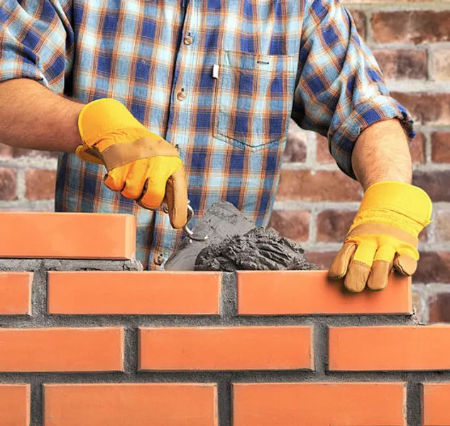 Bricklayer in work gloves laying bricks with a trowel