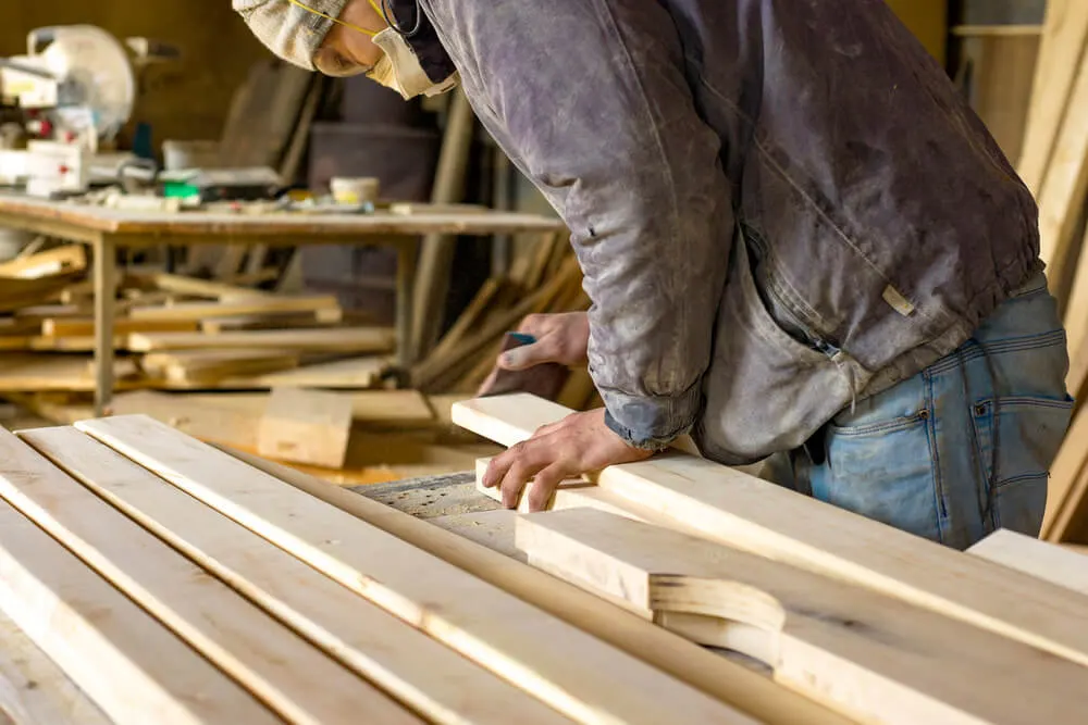Carpenter in a dust mask handling timber boards at a workshop bench